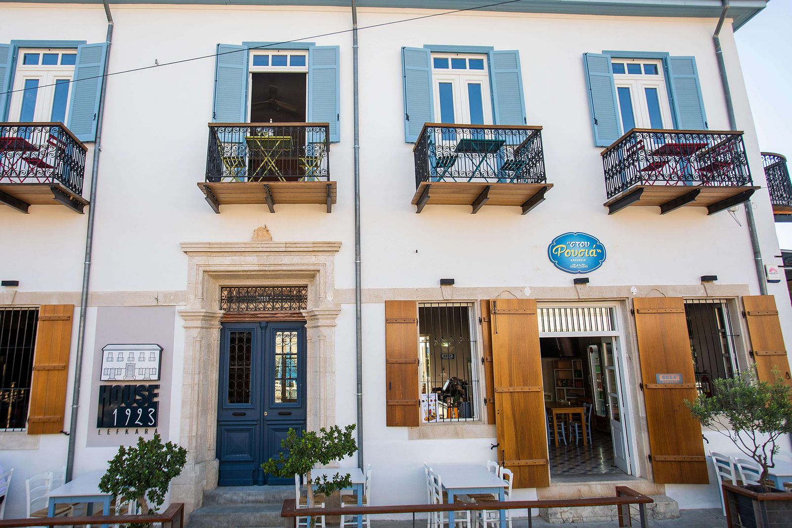 The restored 1923 facade of House 1923, with blue shutters and a cafe terrace, in Pano Lefkara