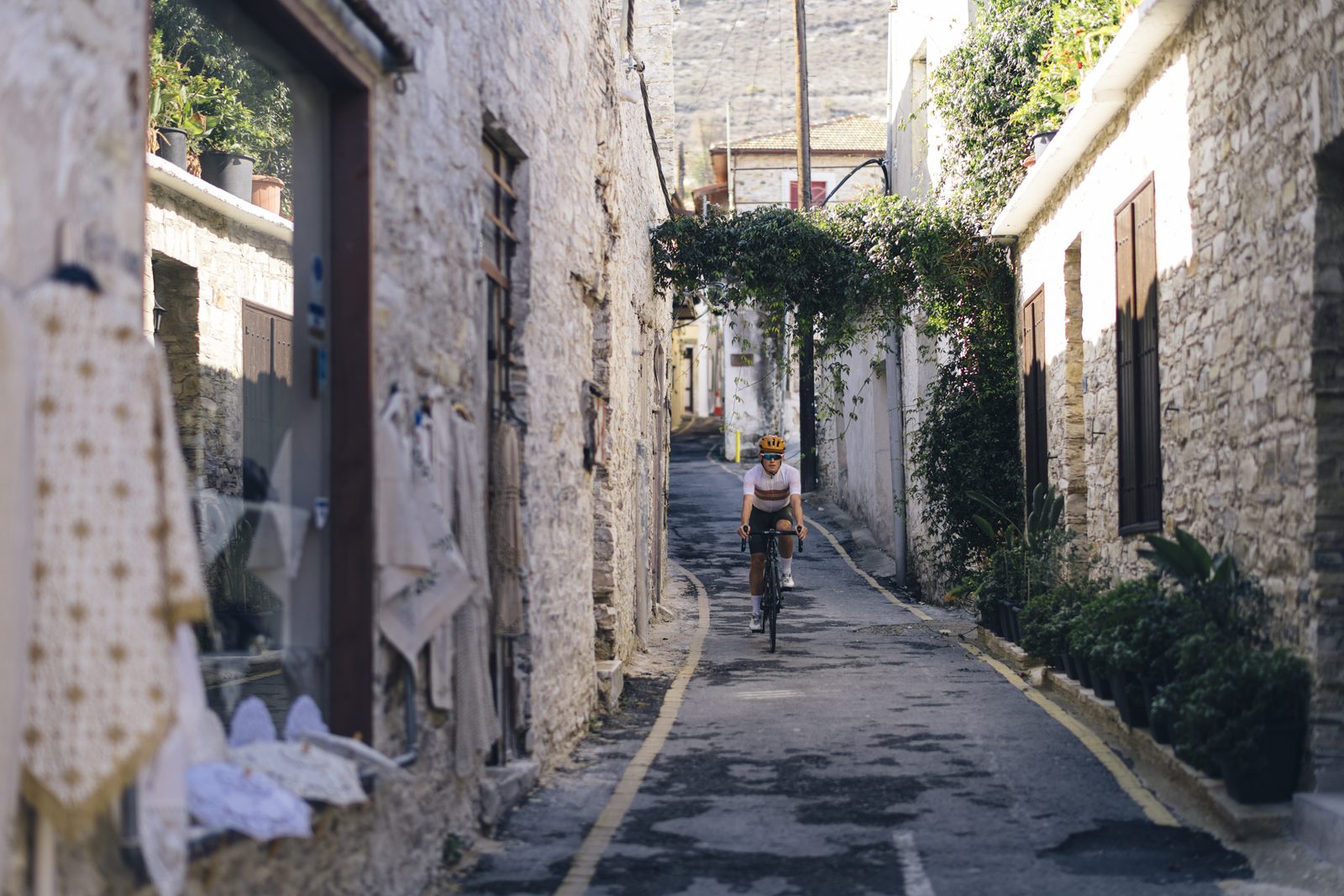 A rider climbs a narrow stone lane in Pano Lefkara, Lefkaritika lace hanging on the walls