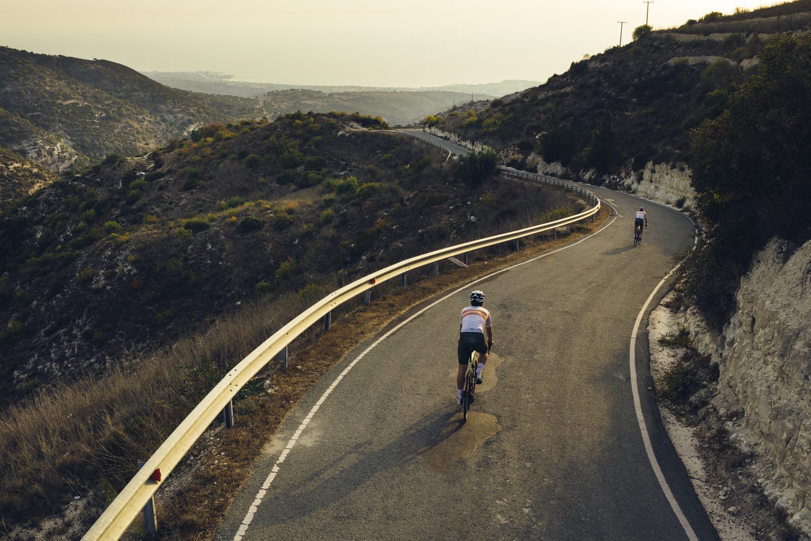 A rider descending a guardrail-lined road toward the distant coast at dusk